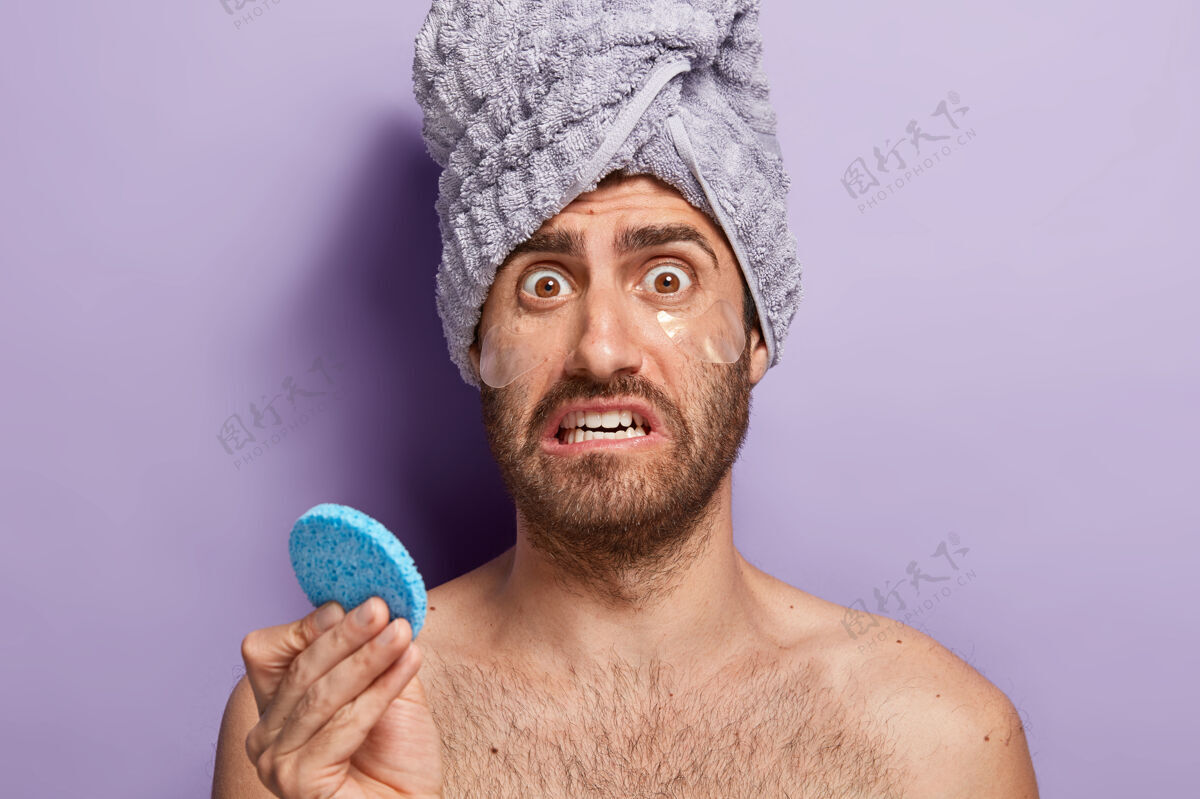 毛巾紧张的男性表情焦虑不安 拿着化妆海绵 敷上水凝胶眼袋贴产品保湿剂紫色