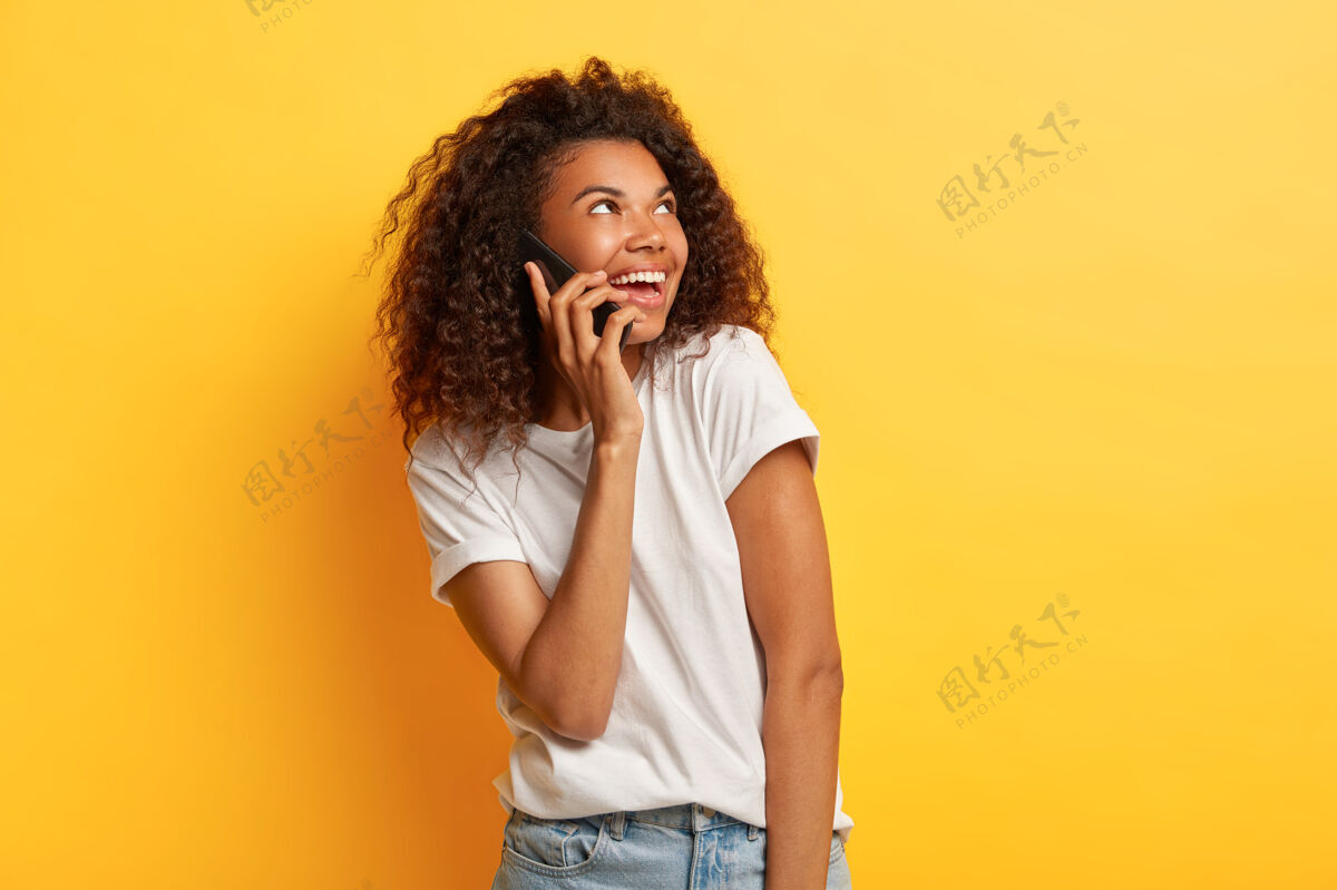 电话美貌知足的美籍年轻女子享受愉快的交谈 把手机放在耳边 看向一旁 穿着休闲的白色t恤模特民族非洲