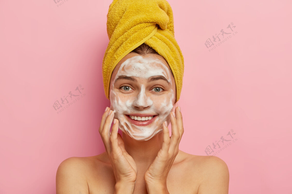 女士洗脸和卫生观念年轻开朗的欧洲女人用肥皂洗脸 用双手触摸脸颊 头上裹着黄色毛巾 表情积极 去除污垢微笑人清洁