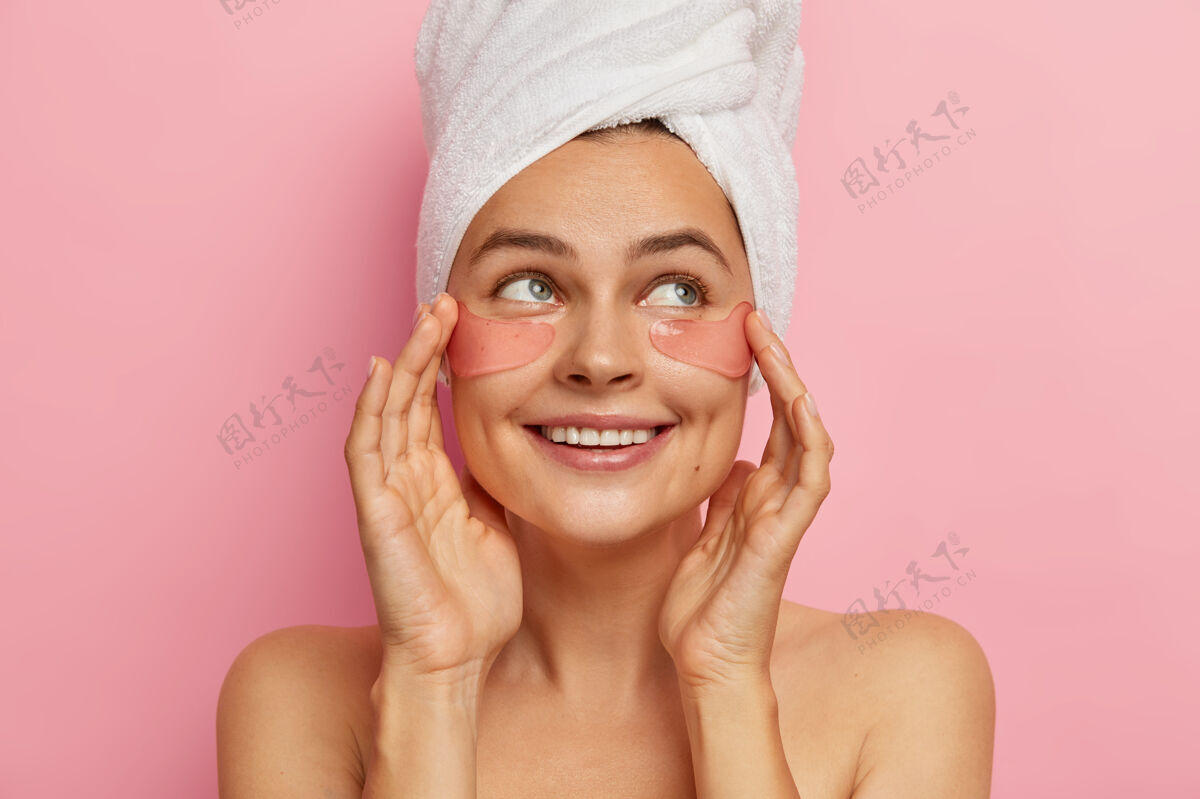 涂抹正面美貌的女人关心眼睛的皮肤美容 在脸上贴上保湿的胶原蛋白贴片 放眼望去 赤裸上身站着 洗澡后做美容 除皱面膜女人粉色