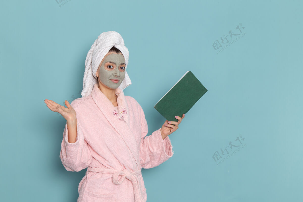 人正面图身着粉色浴袍的年轻女性淋浴后在蓝色墙上阅读抄写本美丽的水浴霜自理淋浴浴室女浴室自理