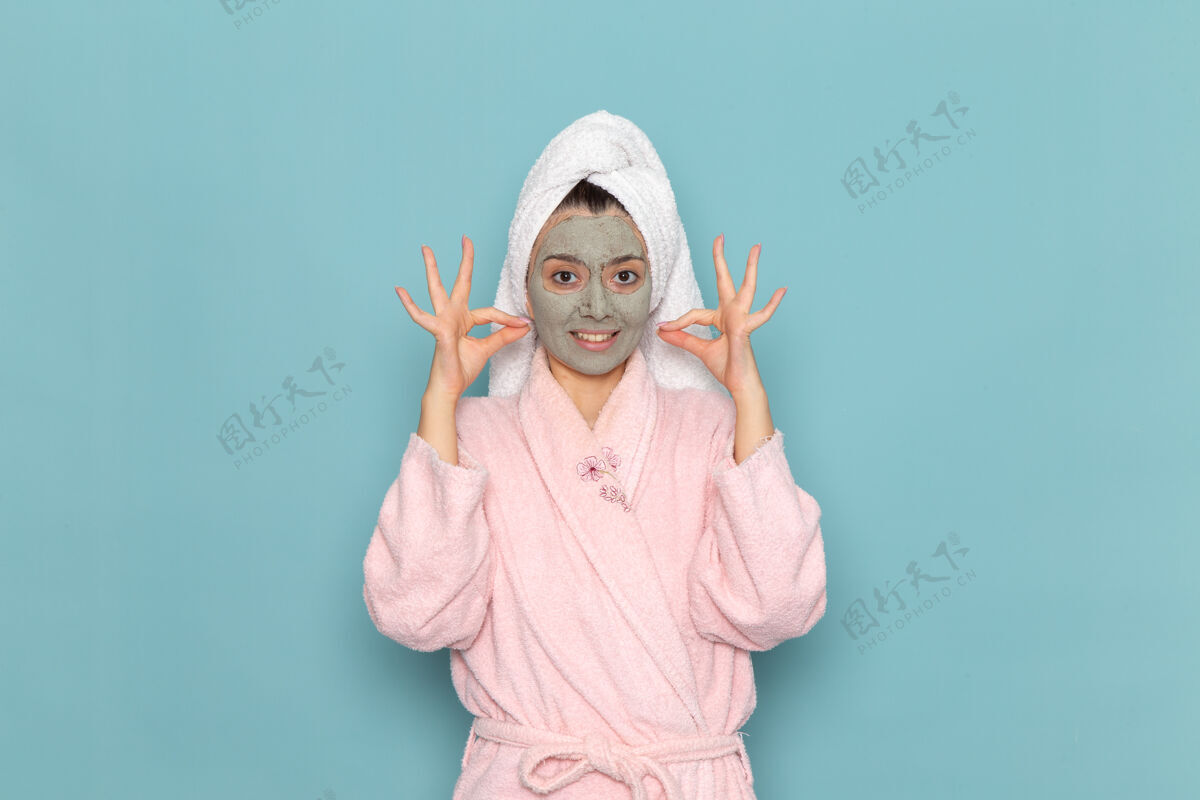面具正面图身着粉色浴袍的年轻女性 脸上戴着口罩 在蓝色墙上清洗美容自护霜淋浴视图男人清洁