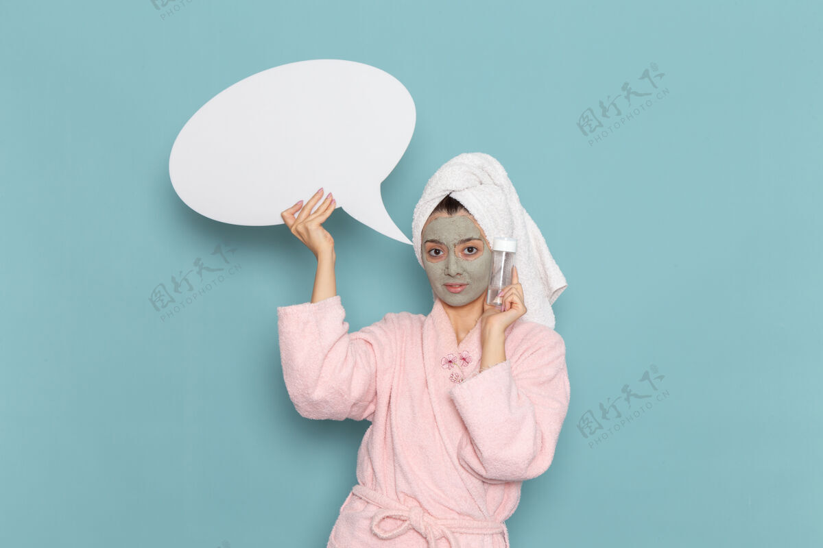 高尔夫正面图年轻女性穿着粉色浴袍淋浴后手持标志 喷在蓝色墙面上的美容水霜自护淋浴浴室举行后视图