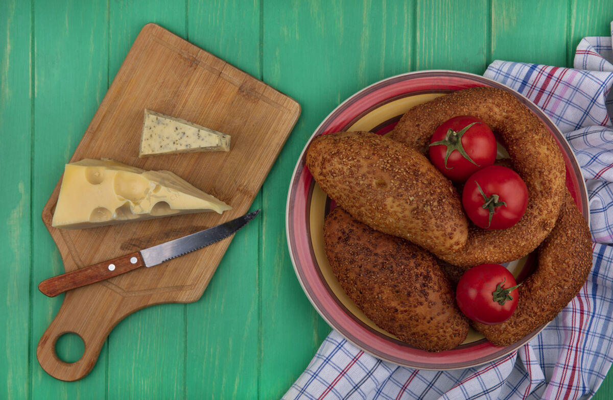 新鲜一个碗上的软芝麻饼的俯视图 新鲜的西红柿放在一块布上 奶酪放在一个木制的厨房板上 刀子放在绿色的木制背景上肉牛肉刀