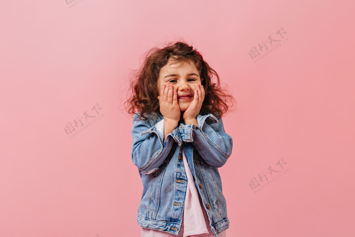 游戏可爱可爱的孩子在牛仔夹克触摸脸微笑的少女在粉红色的背景摆姿势学龄前儿童时尚表情