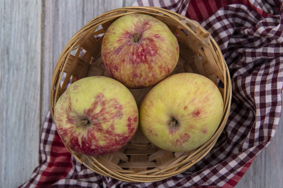苹果灰色背景下格子布上的桶上新鲜多汁苹果的俯视图多汁新鲜水果