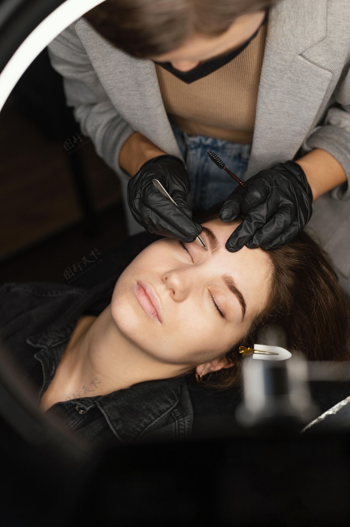 面罩女临床医生为女性做眉毛治疗的俯视图眉毛乳胶手套头发