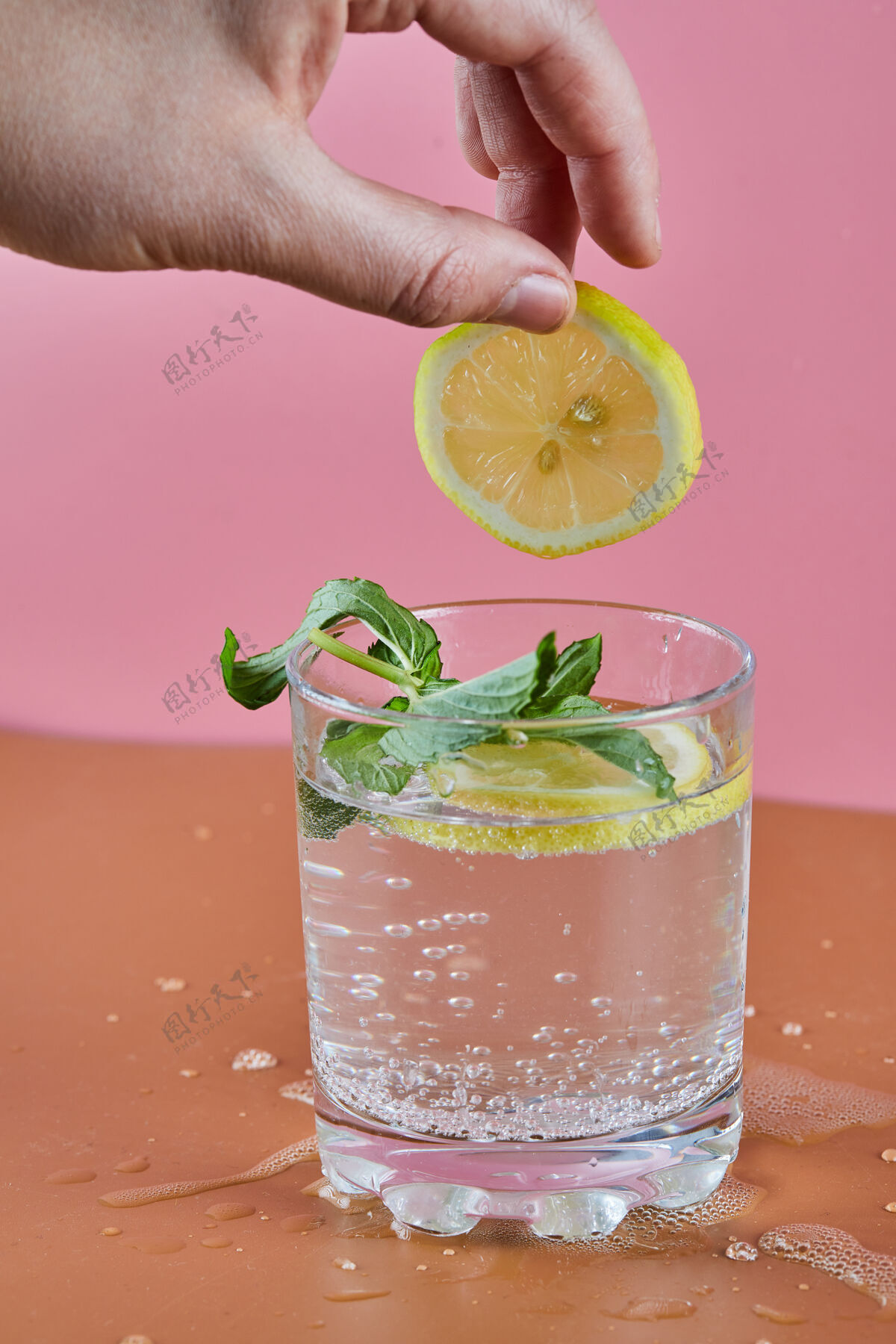 水果一杯清凉的柠檬水放在粉色的表面 女人拿着一片柠檬薄荷水液体