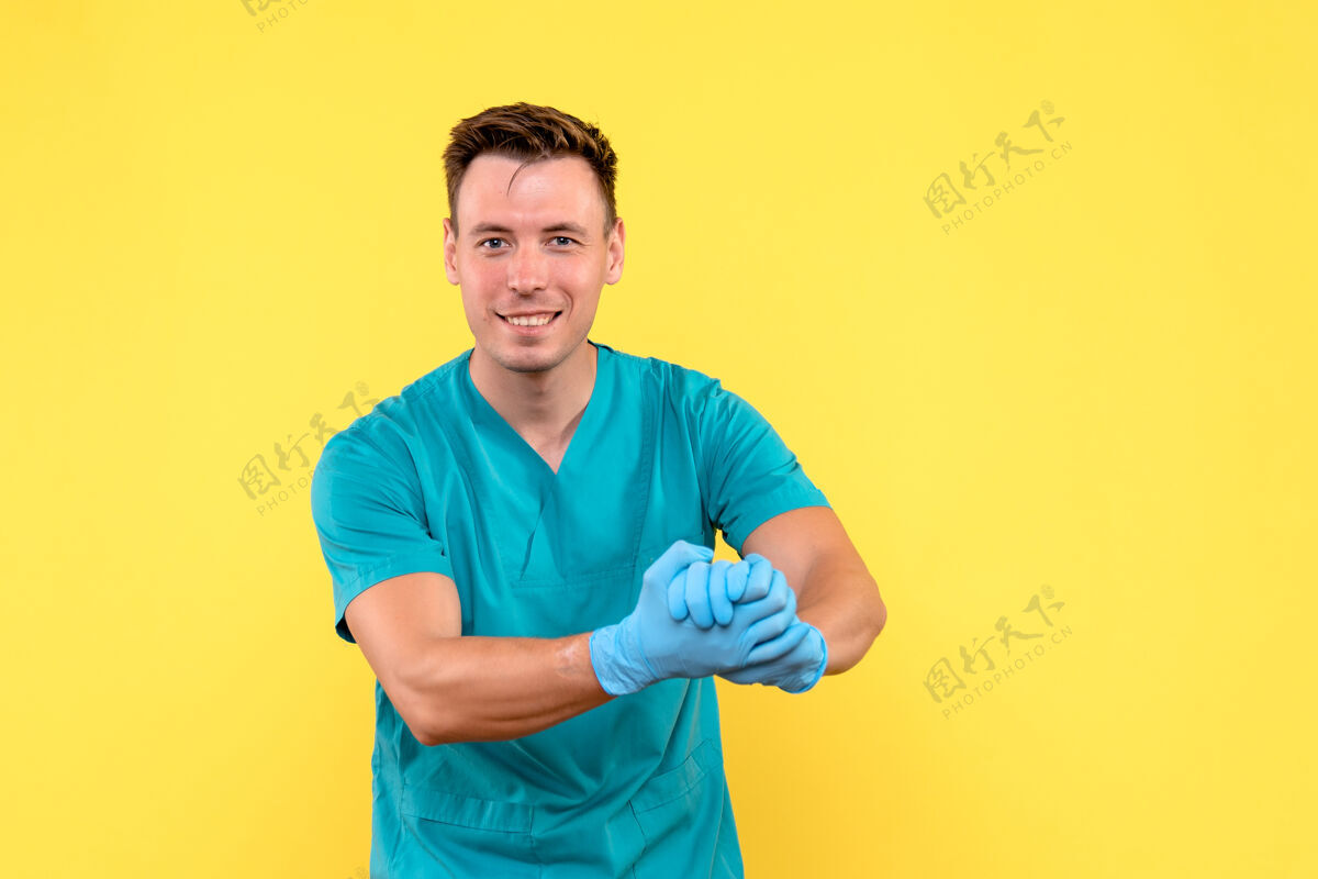 正面黄墙上戴着蓝手套的男医生的正视图微笑医学成人
