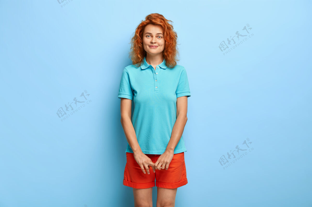 爱情端庄可爱的少女 红色卷发 有着满意的表情 穿着休闲的蓝色t恤和短裤酒窝情感空闲时间