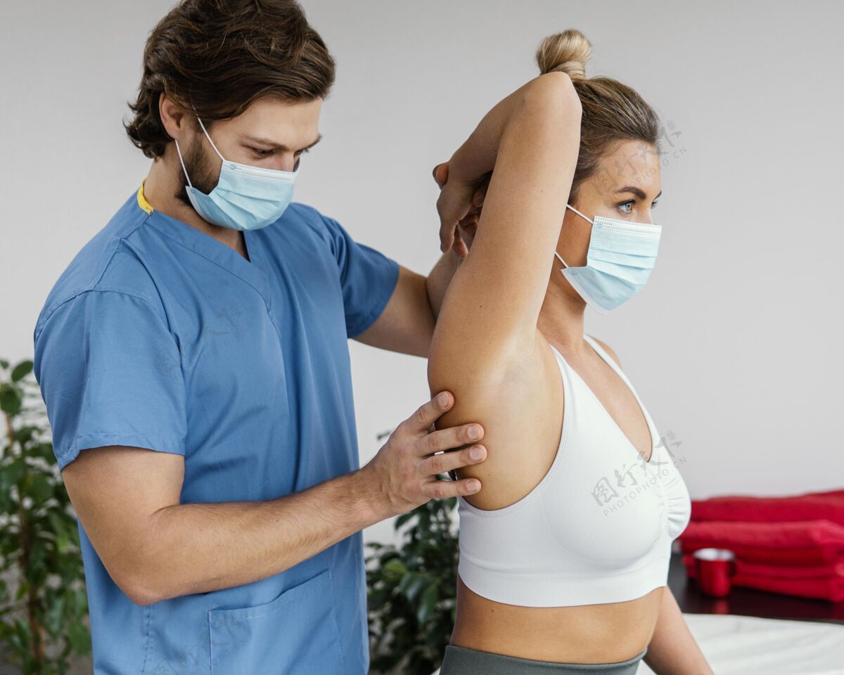 男人男性骨科治疗师带着医用面罩检查女性患者的肩关节女人健康女人