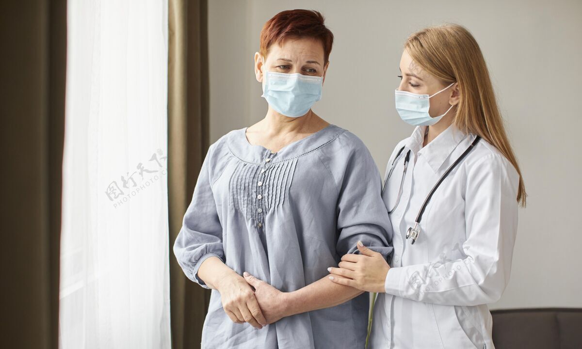 病毒带着医用面罩的老年患者和科维德康复中心的女医生拥抱听诊器治疗老年人