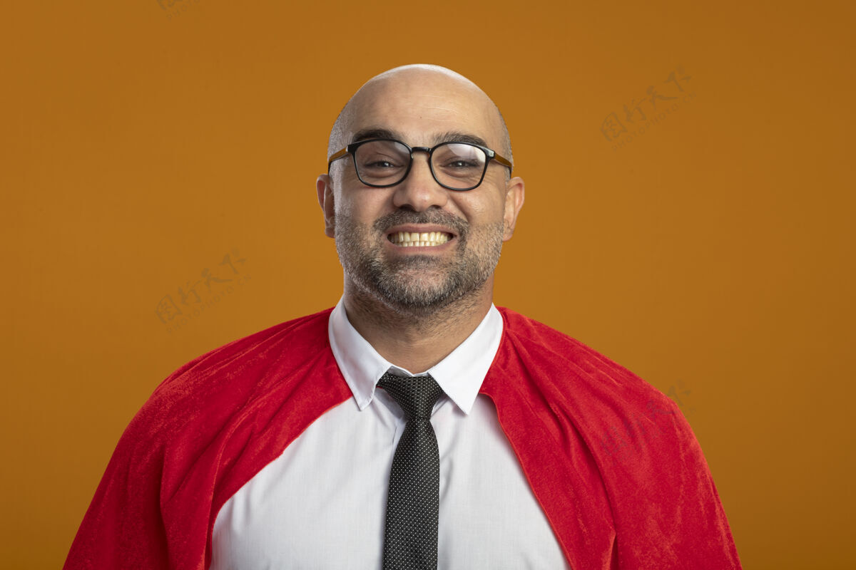 看身穿红色斗篷 戴着眼镜的超级英雄商人站在橙色的墙上 面带微笑 快乐而积极地站在前面人人超级英雄