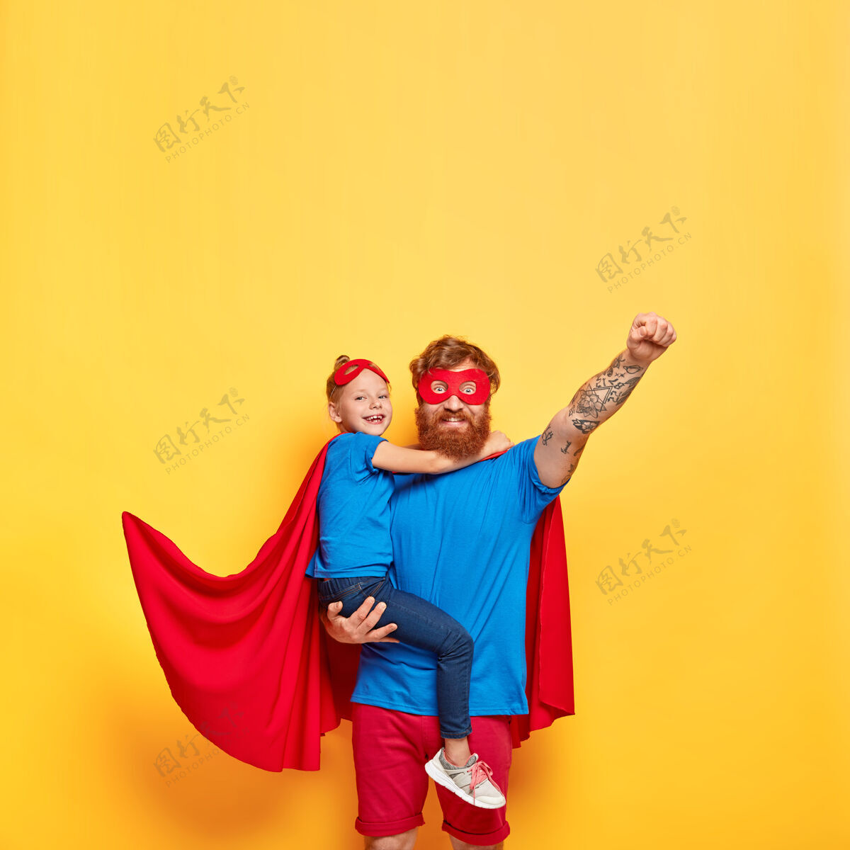 服装穿超级英雄服装的强壮红发男子的垂直镜头 举起拳头 做出飞翔的手势面具父亲身份女儿