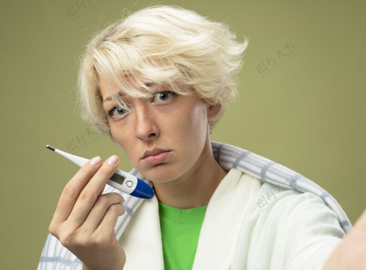 短裤生病的不健康的女人 短发裹在毯子里 身体不适 拿着体温计 表情悲伤 患流感 站在光墙上表情不健康生病