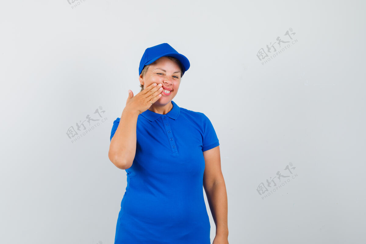 女性穿着蓝色t恤的成熟女人把手按在脸颊上 看起来很高兴帽子活跃可爱