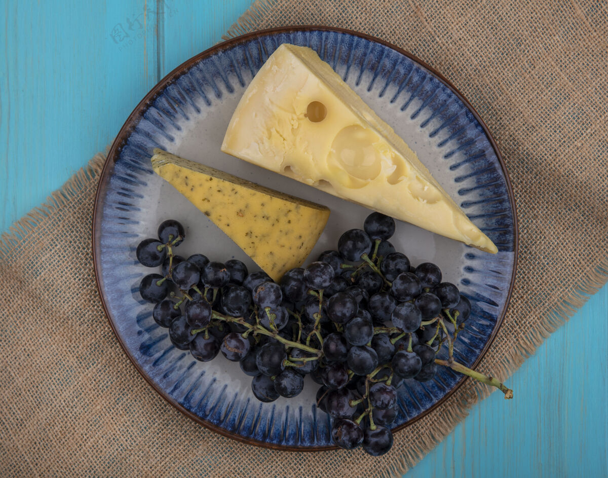 新鲜顶视图黑葡萄和奶酪片放在米色餐巾上的盘子里视野葡萄黑色