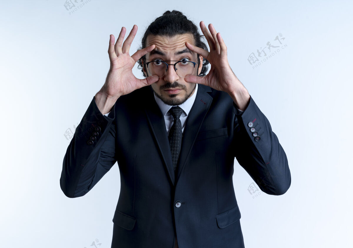 眼睛一个穿着黑西装戴着眼镜的商人站在白墙上试图睁大眼睛看眼镜西装