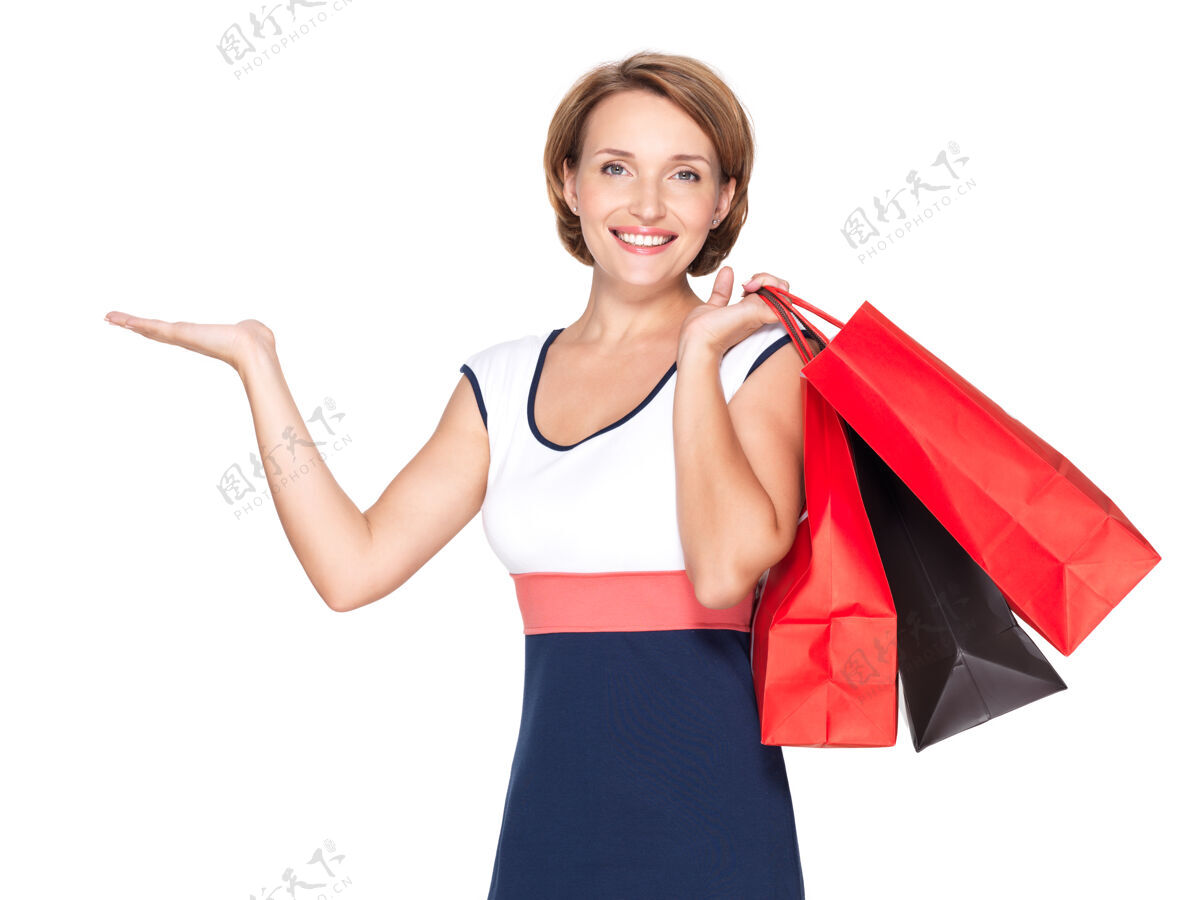 正面一个美丽的快乐的女人的肖像与介绍姿态和购物袋超过白墙点年轻成人