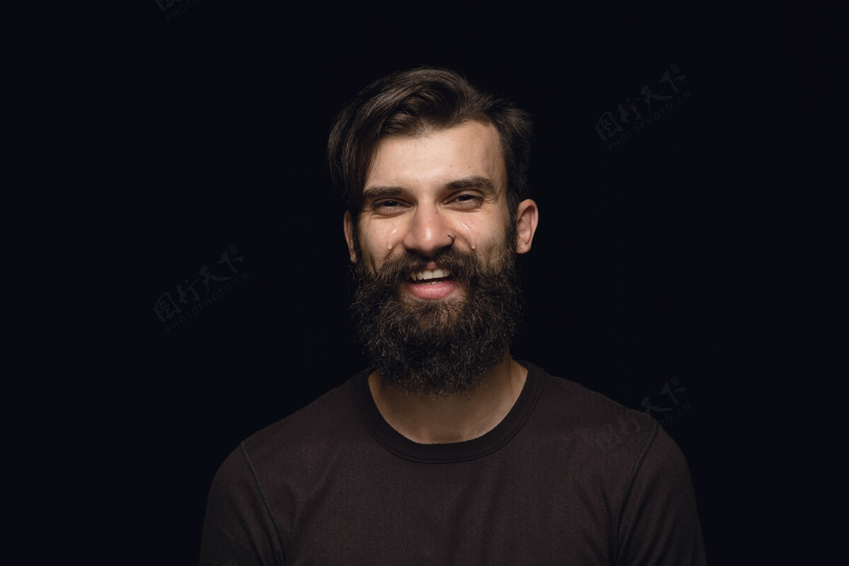公司在黑色工作室背景上拍摄的年轻人的特写肖像男模特真实情感的照片笑中哭面部表情 人类情感概念笑优雅微笑