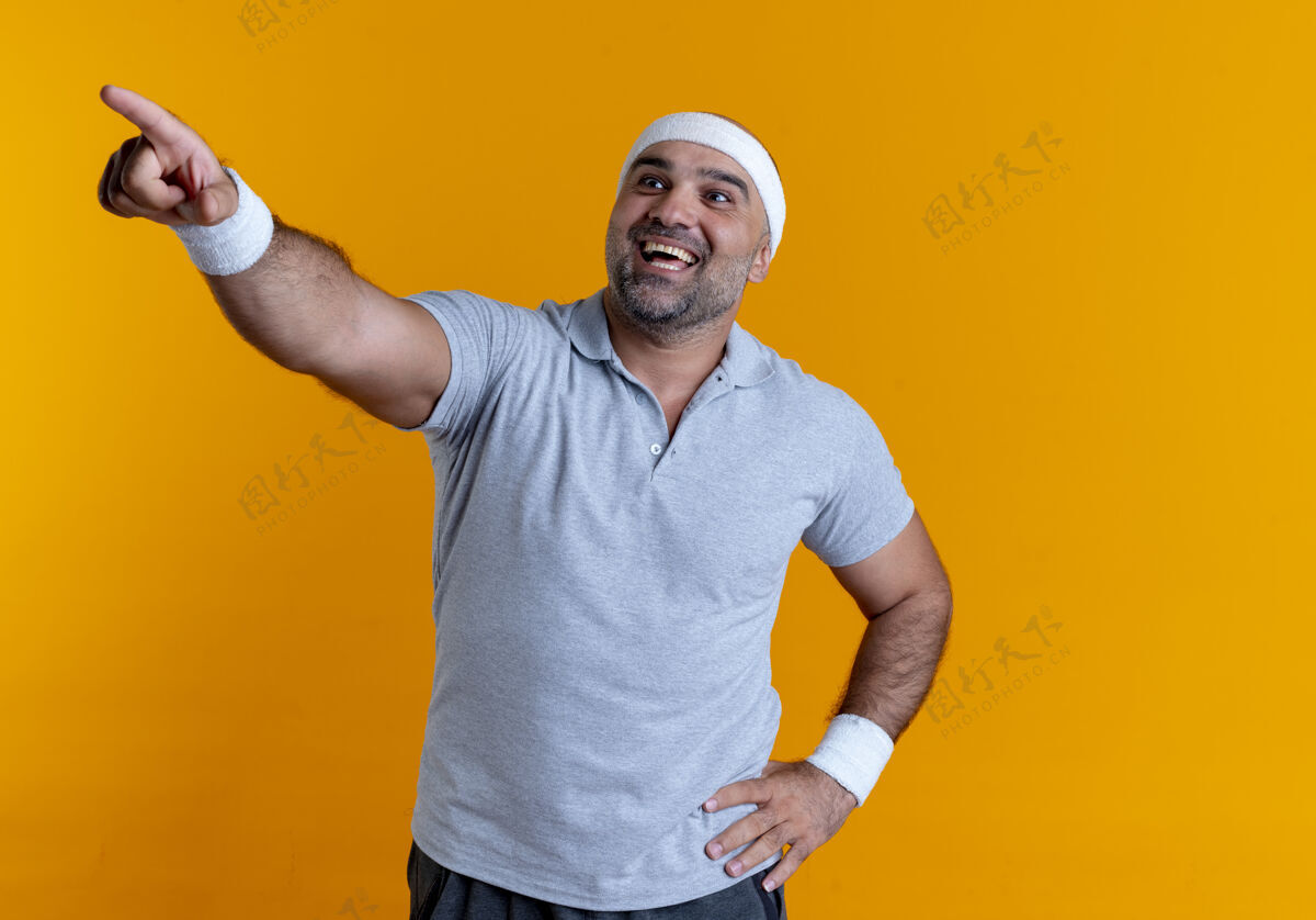 看戴着头巾的成熟的运动型男人看起来很自信 微笑着用手指着站在橙色墙上的一边男人公民运动装