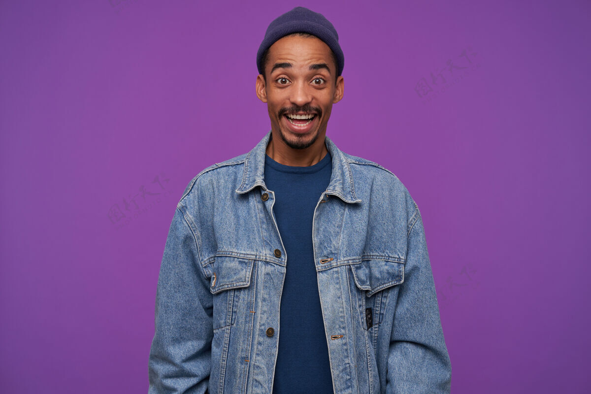 毛衣室内镜头：年轻快乐的黑皮肤男性 留着胡须 表情激动 眉头高抬 笑容满面 在紫色的墙上摆姿势胡须积极情绪