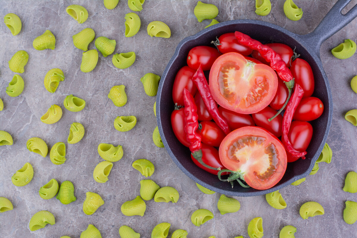质量把樱桃番茄和红辣椒放在一个黑锅里 周围是绿色的意大利面菜单厨房餐厅