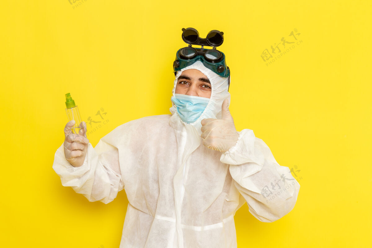 面具正面图身穿特殊防护服的男科学工作者手持喷雾瓶在淡黄色的表面上喷雾套装手持