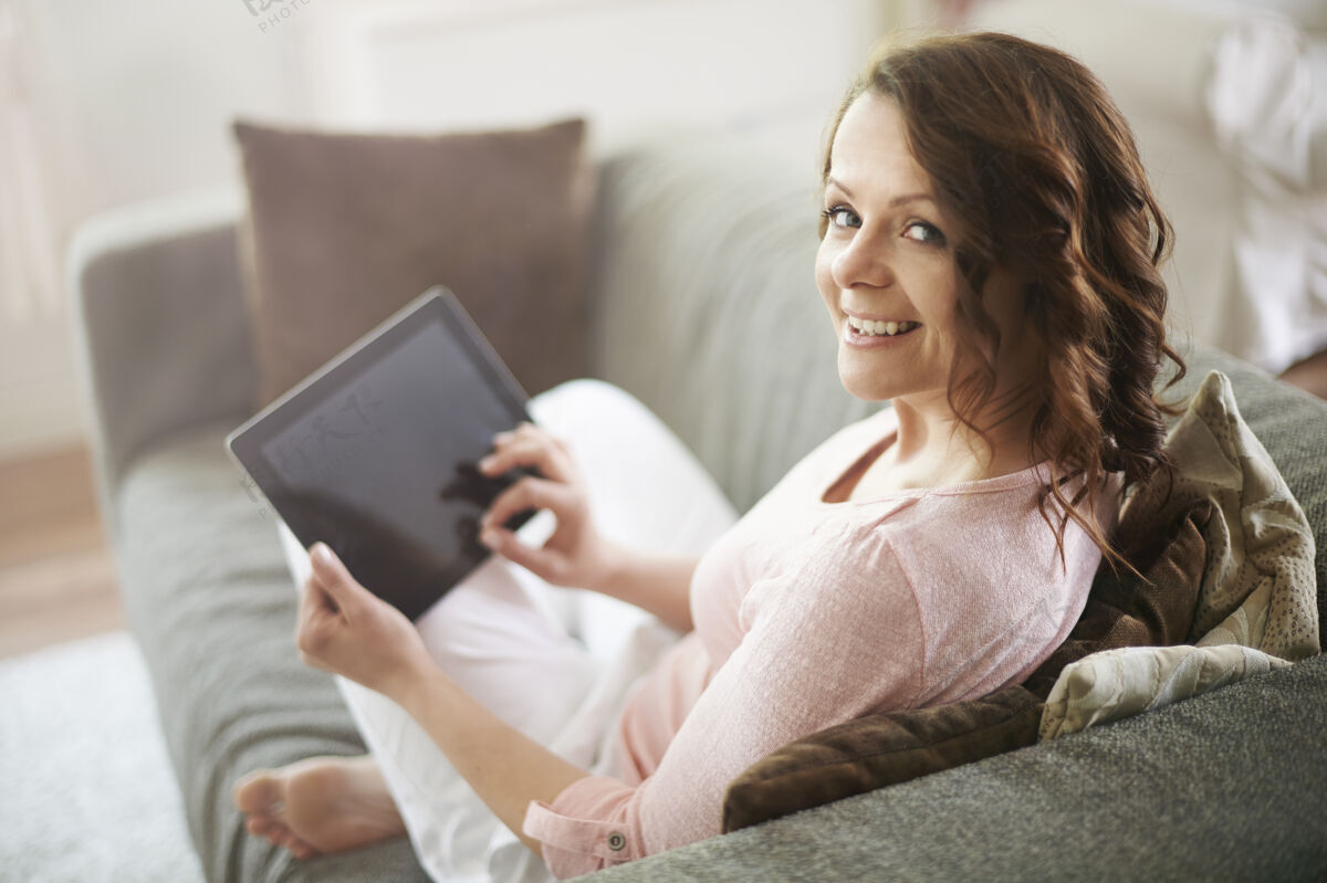 触摸坐在沙发上用平板电脑的女人互联网坐着室内