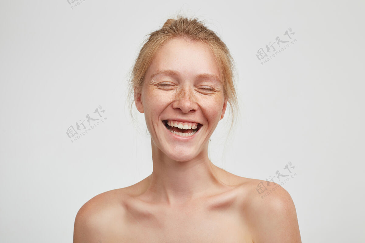 发髻容光焕发的年轻快乐的红发女人闭着眼睛 开心地笑着 站在白墙上 精神高昂女性发型发型