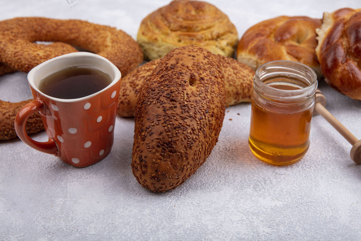 罐子侧视图美味芝麻饼与一杯茶和蜂蜜的玻璃罐和不同的面包隔离在一个白色的背景美味杯子牛肉