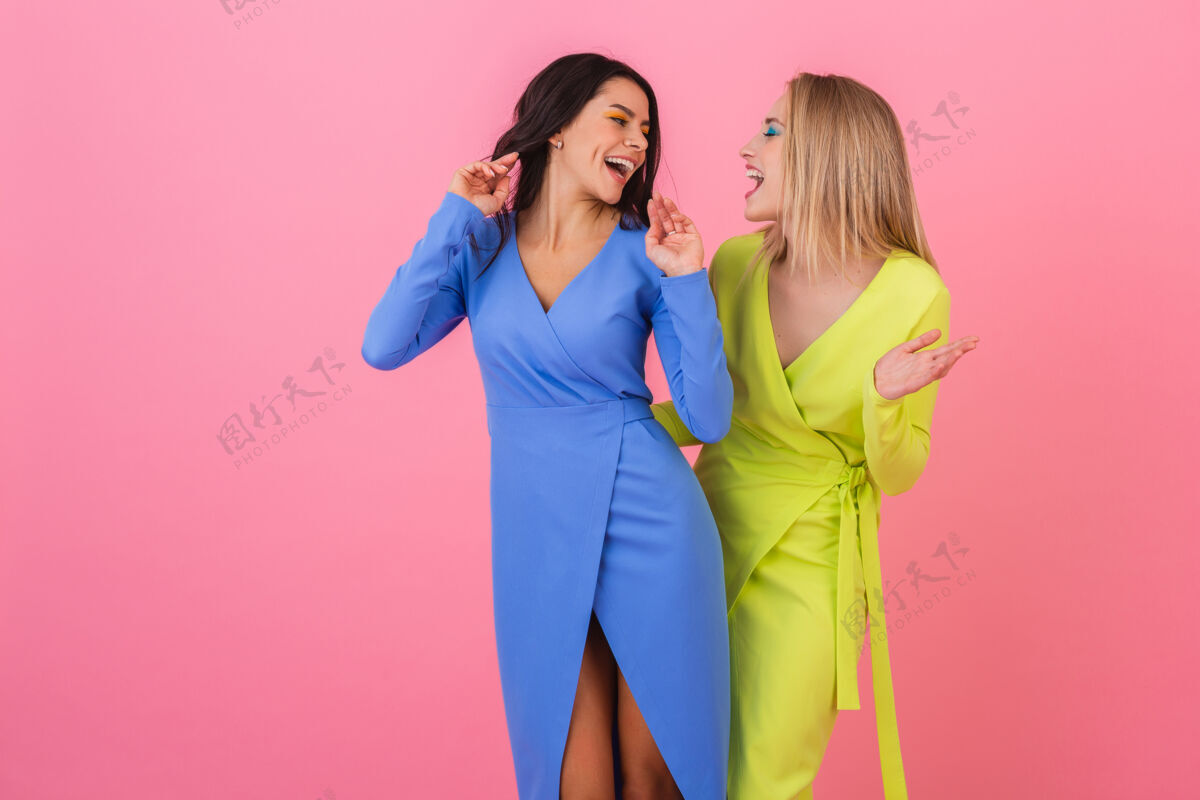 休闲两个时尚的微笑迷人的女人在粉红色的墙上摆着有趣的姿势 穿着蓝色和黄色的时髦多彩的裙子 春天的流行趋势春天女士夏天