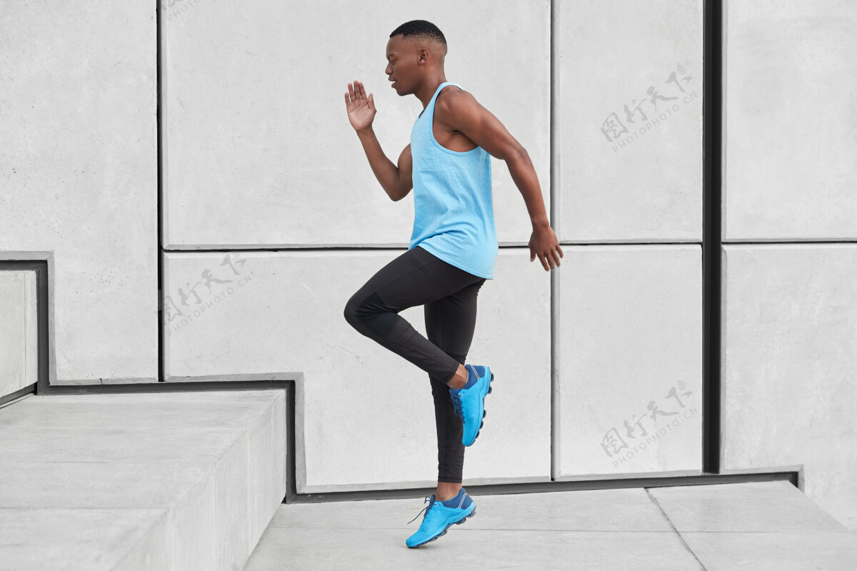 运动鞋坚定的美国黑人运动员侧身向上跑 目标是克服呼吸困难 穿着背心和运动鞋 在白墙上摆姿势运动员运动的年轻人跳在台阶上运动运动员活动