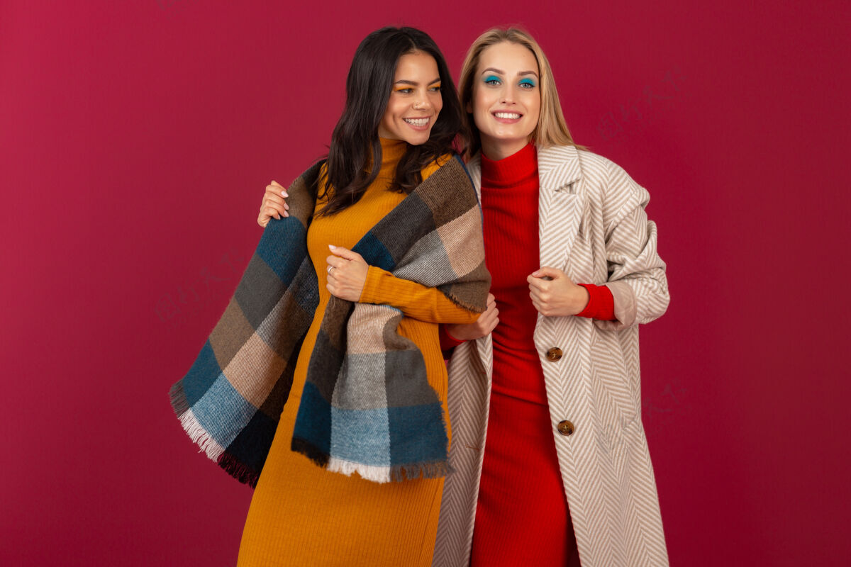 魅力两位笑容可掬的时尚女性穿着秋冬时装和外套 在红墙上孤零零地摆着姿势女人金发时尚