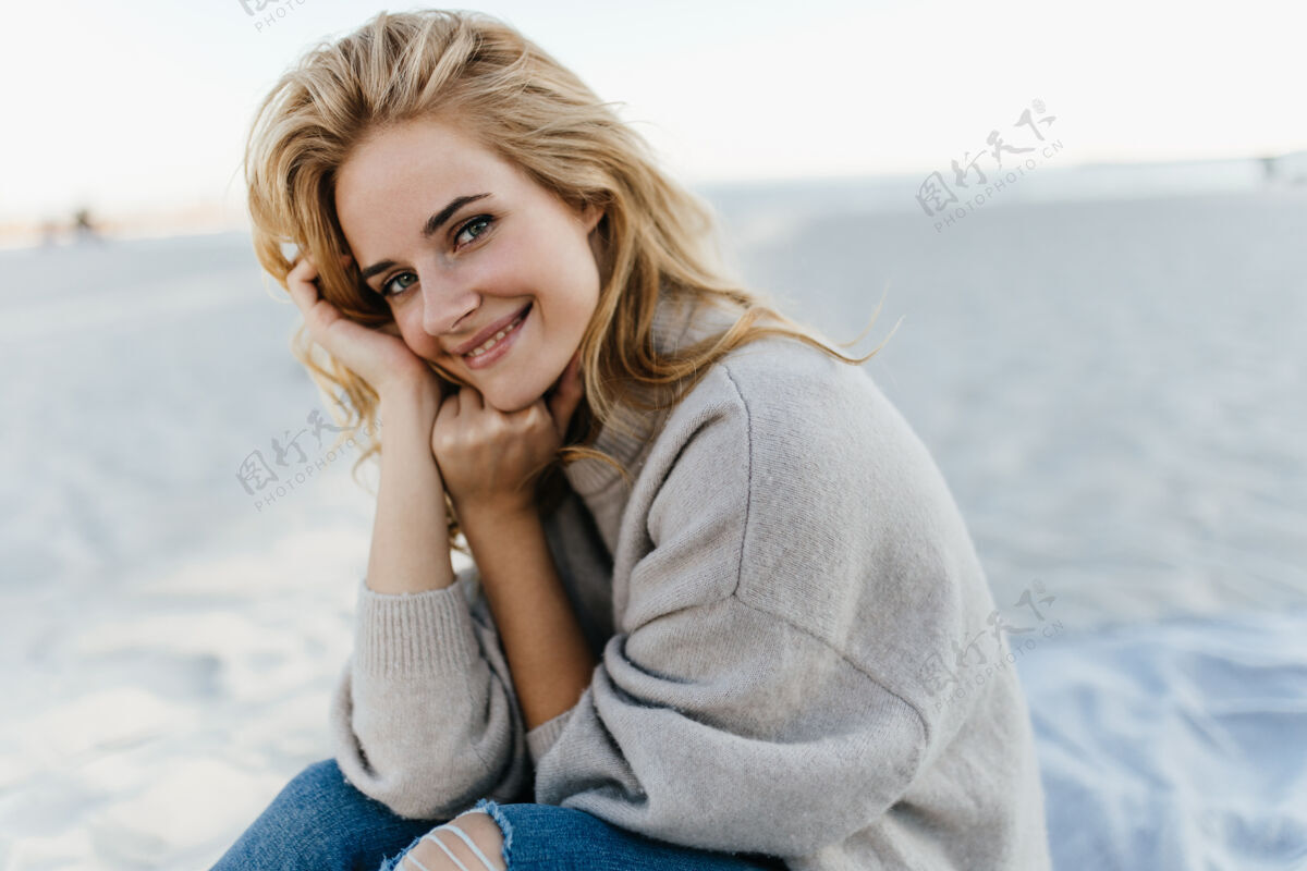 假期一位迷人的年轻女子 一头盲发 穿着羊绒衫 坐在沙滩上享受春日休息欢笑海景