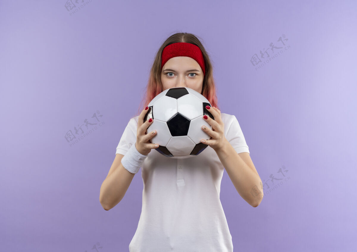 运动年轻的运动型女子拿着足球躲在球后面站在紫色的墙上站着女人足球