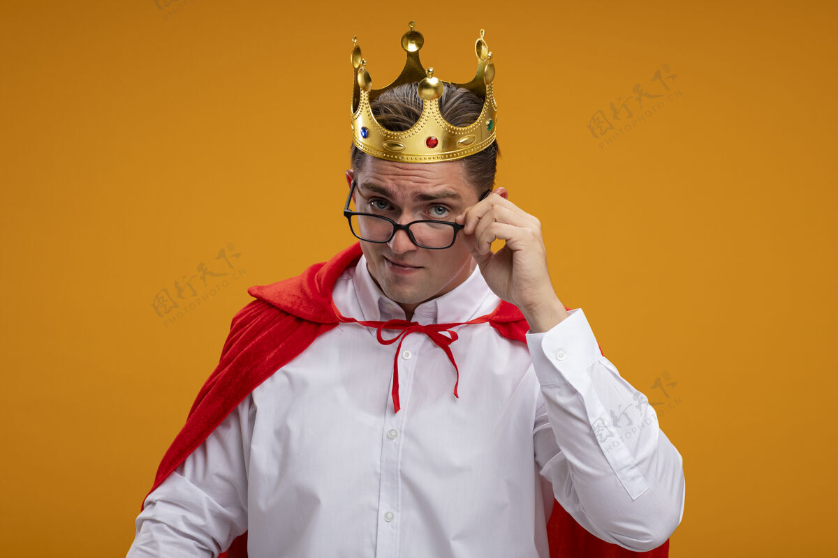英雄身着红色斗篷 戴着皇冠眼镜的超级英雄商人站在橙色背景下 看着镜头被吸引住了超级站着眼镜