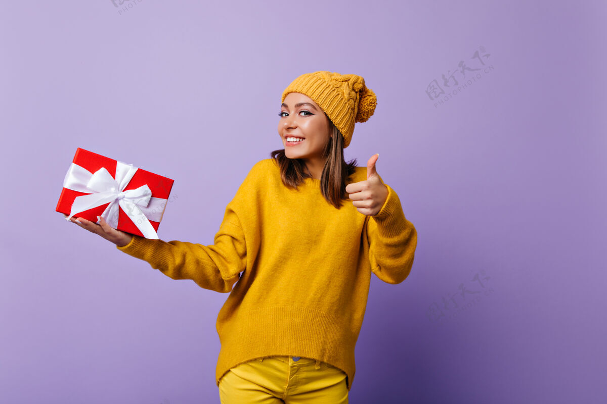 积极快乐的女士戴着时髦的黄色帽子和生日礼物跳舞高加索女孩拿着紫色的新年礼物大笑欢乐幸福生日
