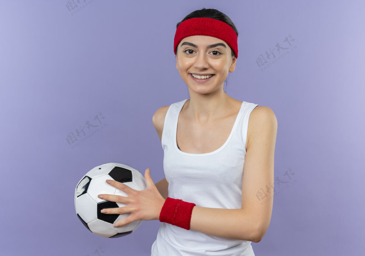 自信身穿运动服 头箍 手持足球 微笑 自信 快乐 积极向上的年轻健身女孩站在紫色的墙上运动装女孩积极
