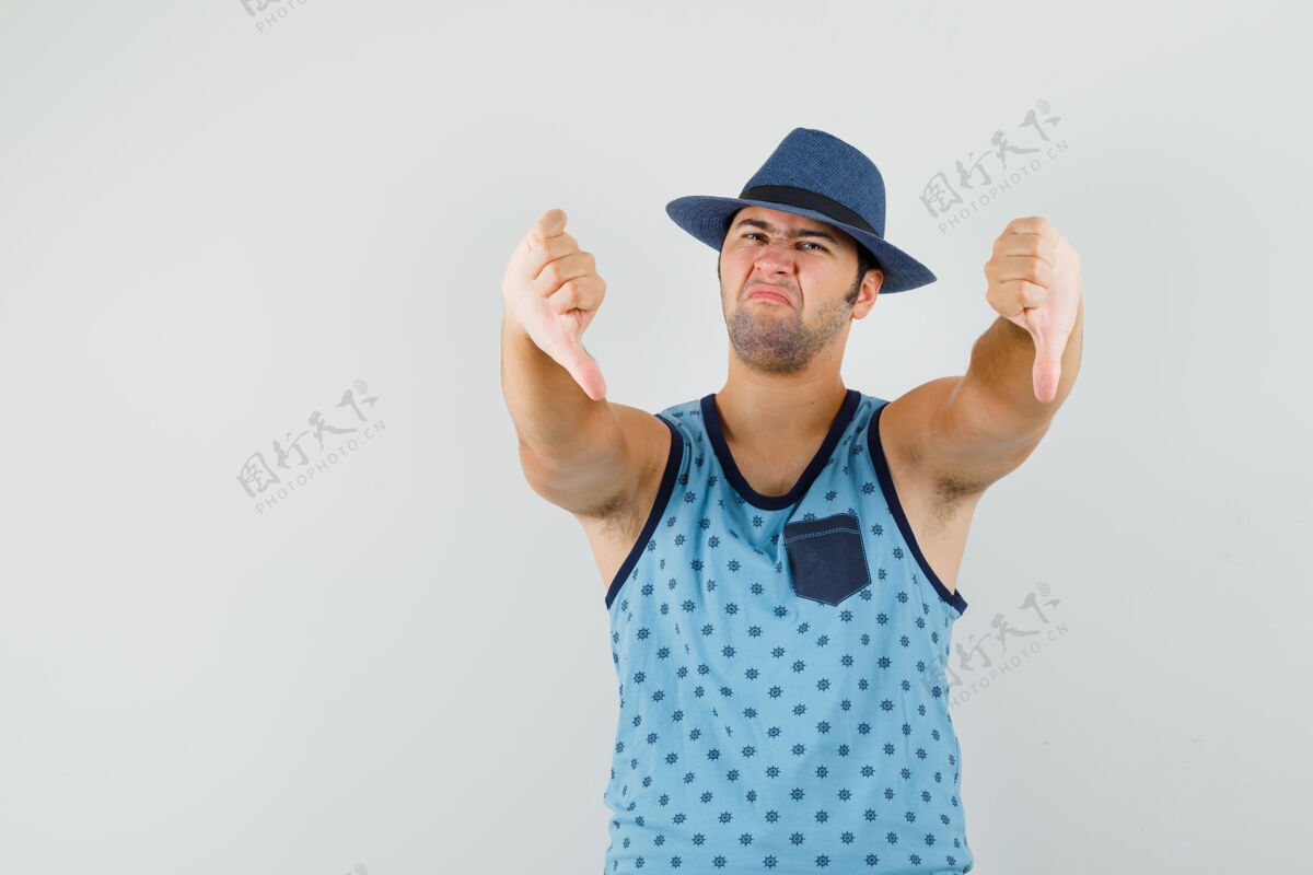 单身年轻人在蓝色的单打 帽子和看起来不满意 前视图双拇指向下休闲微笑朋友
