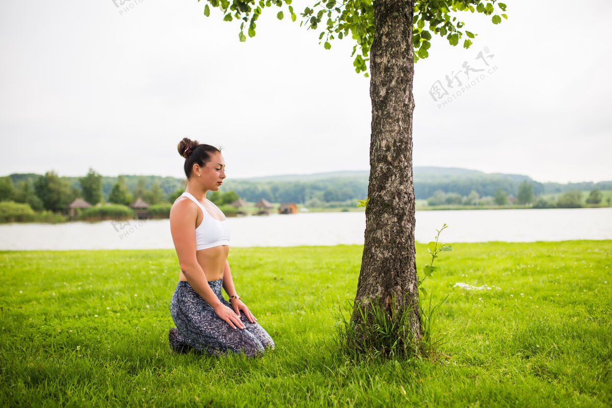 运动年轻健康的女人在湖边和树边的公园里做瑜伽禅宗健康美容