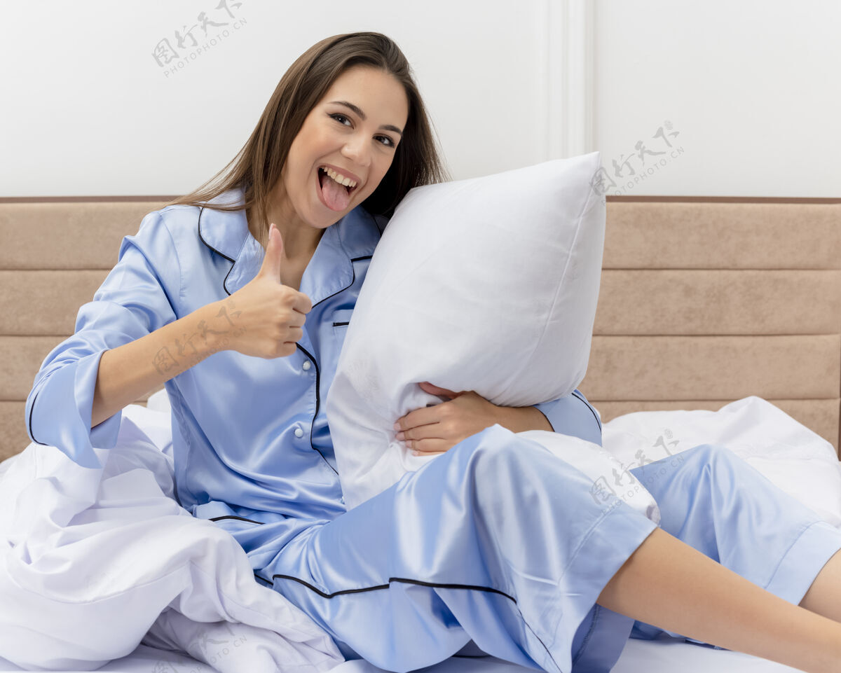 快乐穿着蓝色睡衣躺在床上的年轻漂亮女人坐着微笑卧室