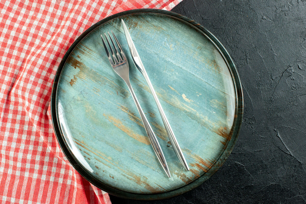 叉子上近距离看钢叉和餐刀在圆盘子上红白格子桌布在黑桌子上圆盘子托盘顶部
