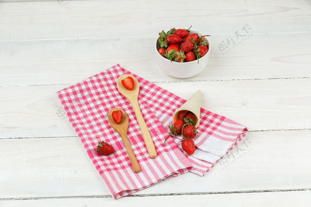 冰把木勺子和草莓放在红色方格桌布上 把一碗草莓放在白色木板上水平清爽奶油桌子