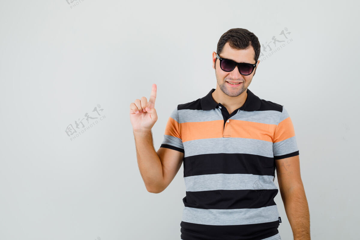 自信年轻人指着上面的t恤衫 太阳镜 看起来很自信前视图帅气发型男人