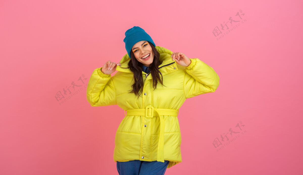 女士迷人的活跃女模特在粉色的墙上摆着鲜艳的黄色冬季羽绒服 温暖的外套时尚潮流羽绒服肖像套装