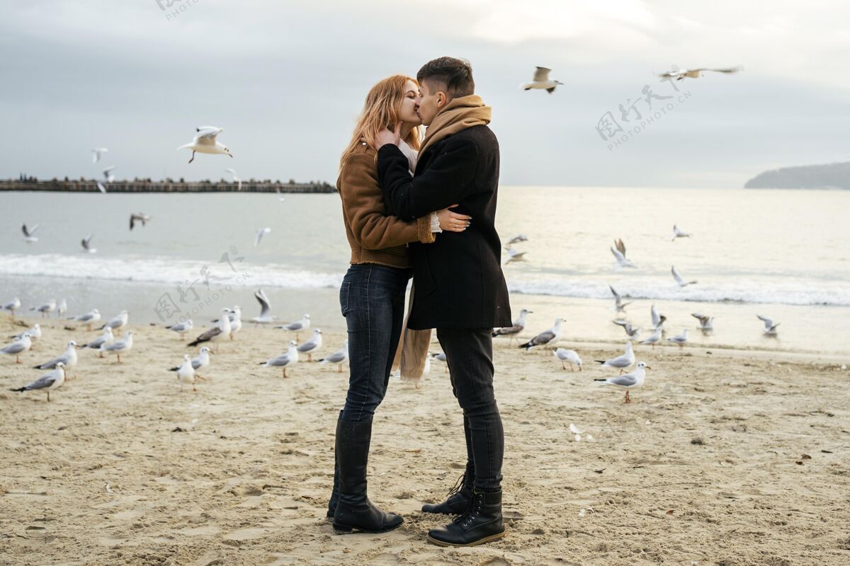 鸟冬天在海滩边接吻的年轻夫妇的侧视图女人探索业余爱好