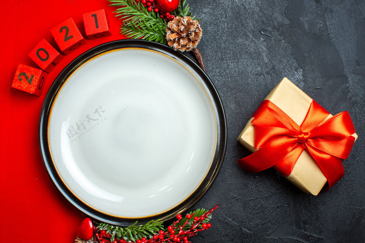 圣诞节新年背景与餐盘装饰配件杉木枝和数字和礼物在一个黑色的桌子上红色餐巾碗厨具冷杉