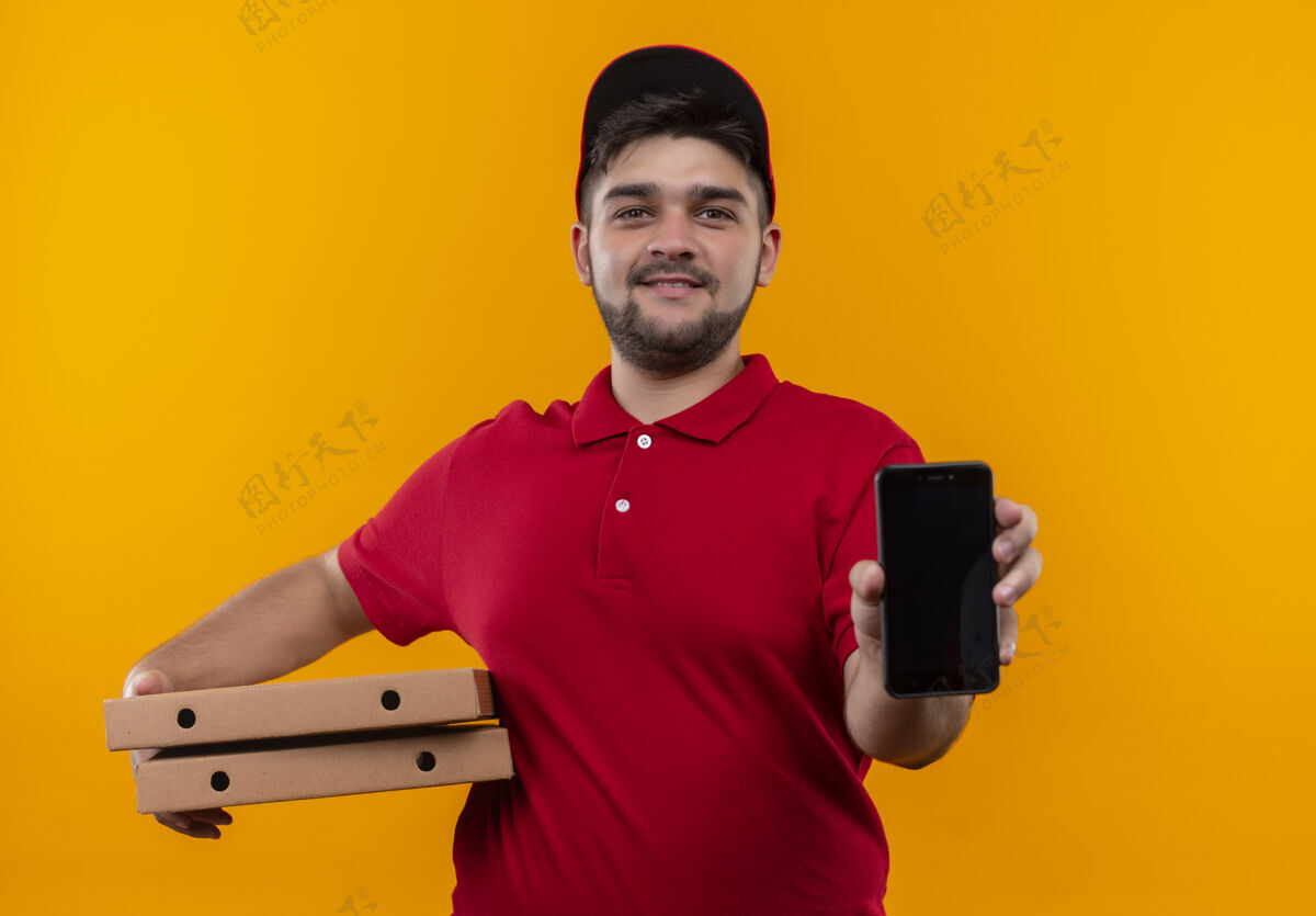 微笑年轻的送货员穿着红色制服 戴着帽子 手里拿着一叠比萨饼盒 脸上露出友好的微笑橙色拿着年轻人