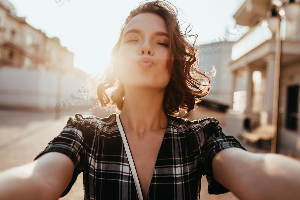 女人浪漫的女孩在阳光温暖的日子里自拍可爱的欧洲女人站在街上亲吻的表情肖像年轻寒冷